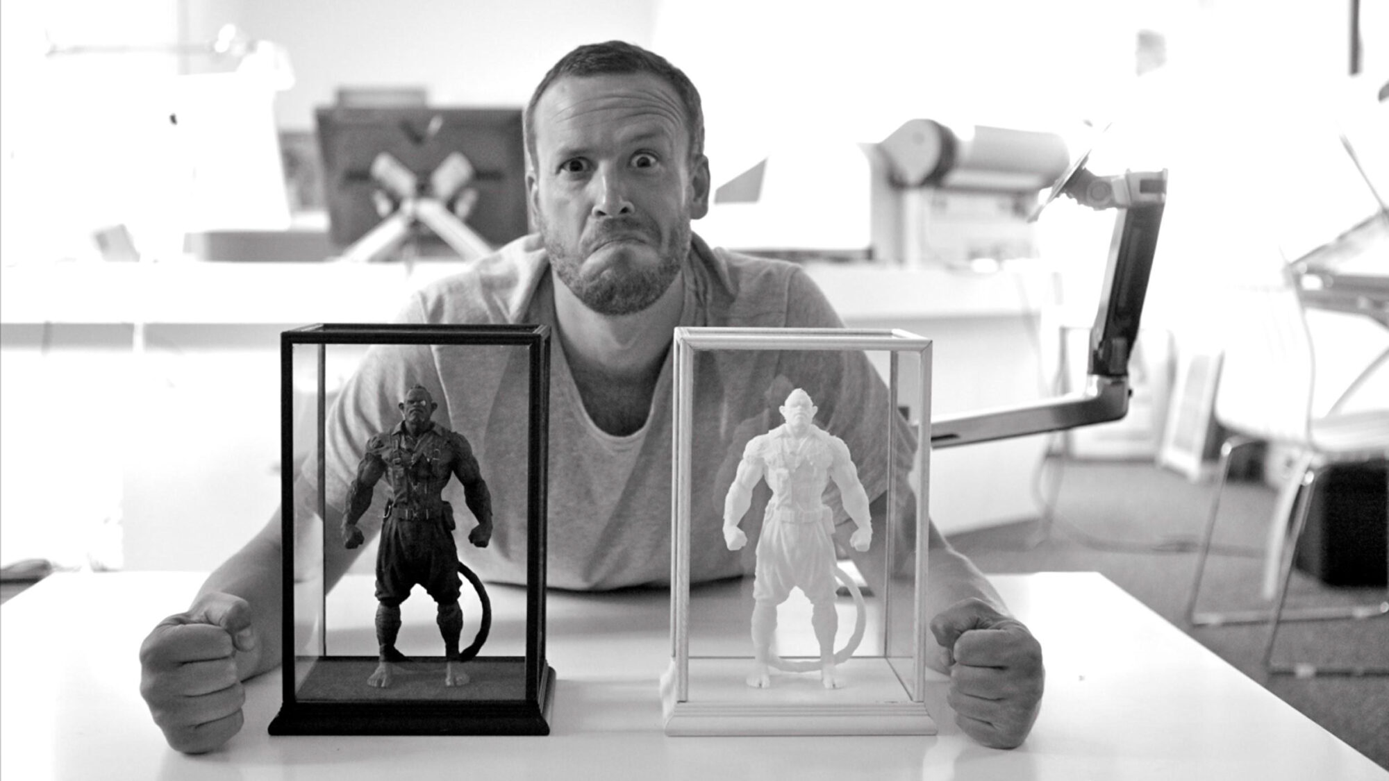 A man sitting at the desk with two small models of the Mono characters