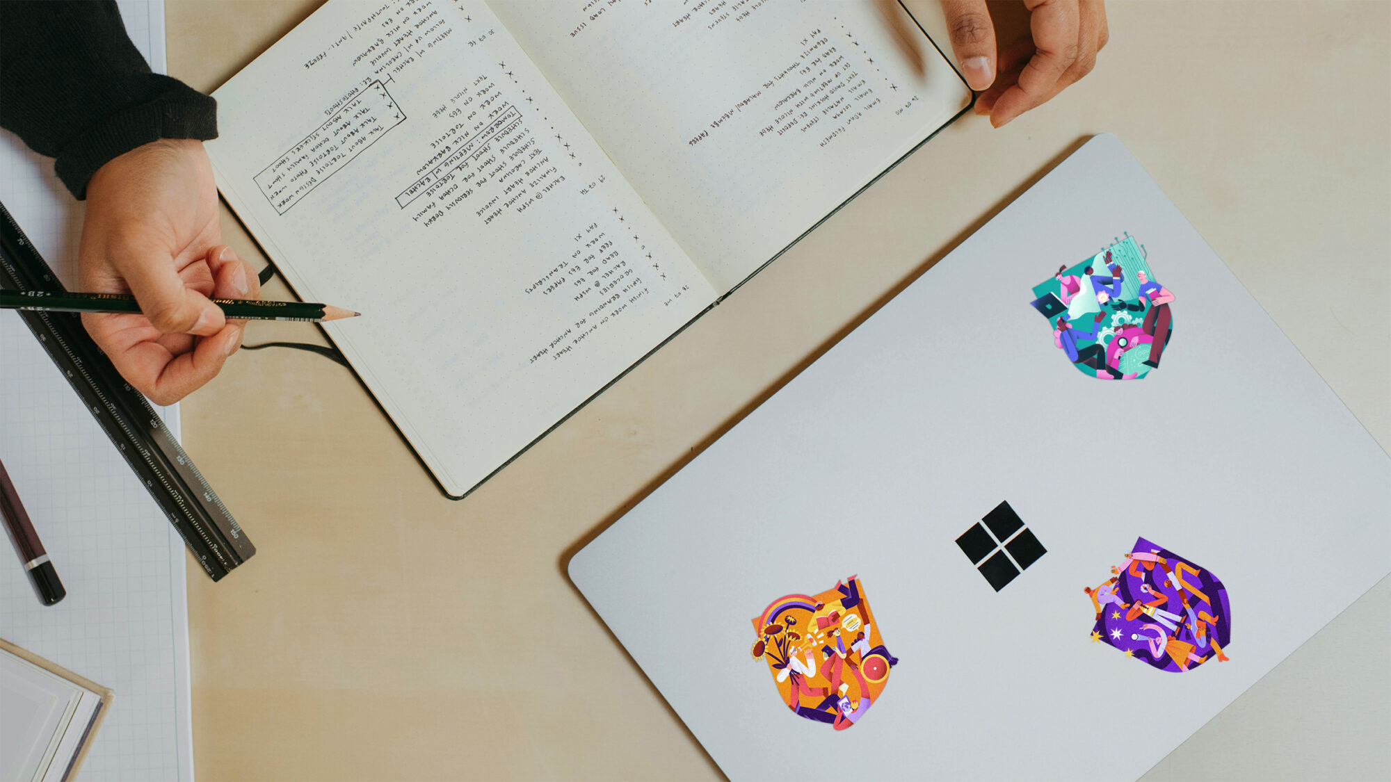 A top down view of someone's desk while they're reading a book. Next to the book is a laptop with Cambridge university stickers.