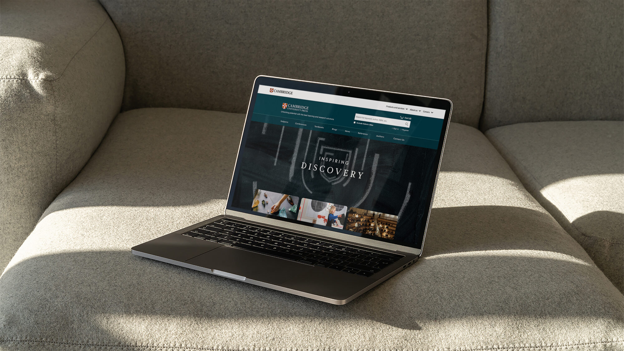 A laptop on a sofa showing the Cambridge Press website.